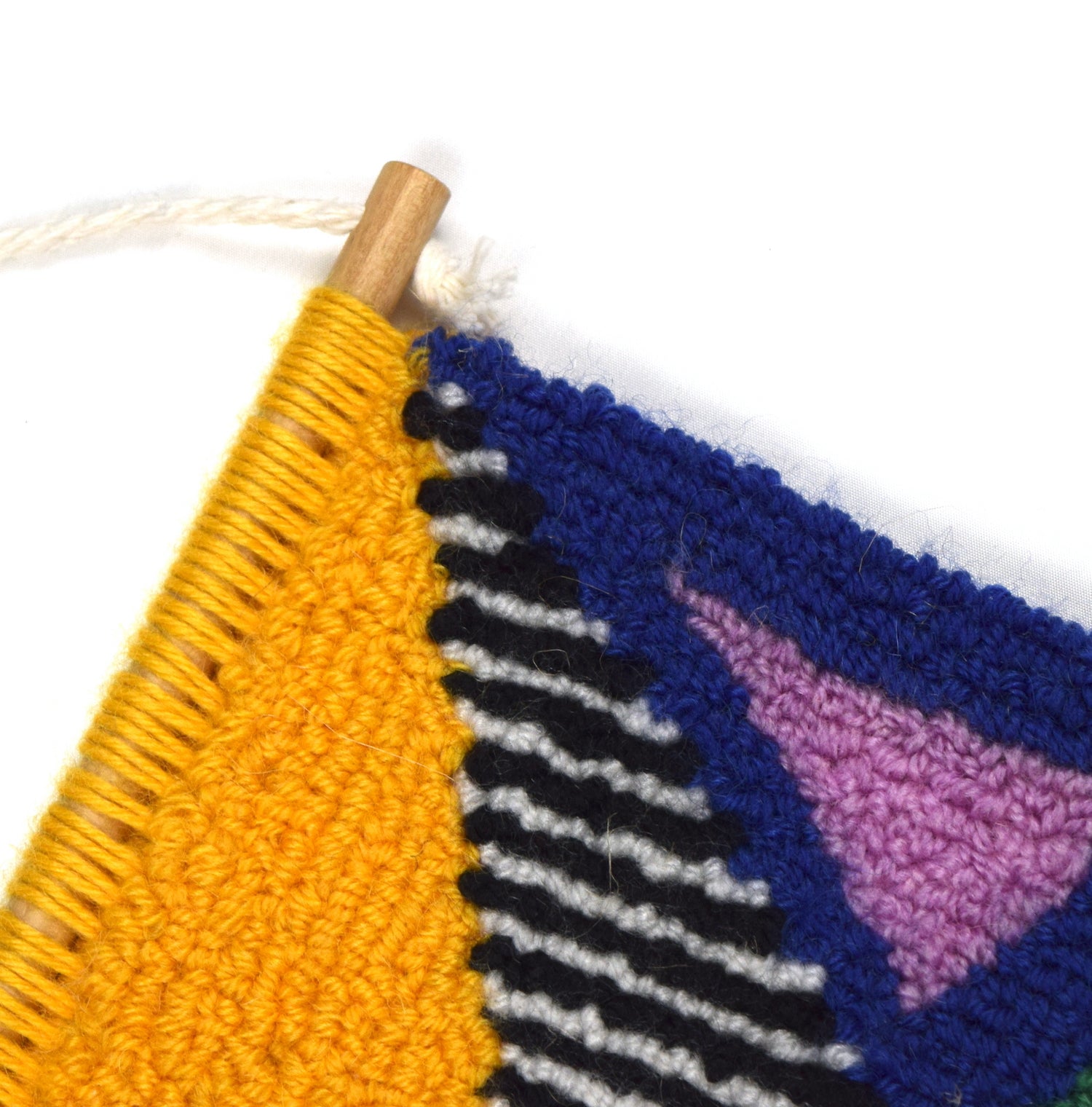 A contemporary hand punched miniature, using yellow, blue, pink, green, orange and purple triangular block colours accented by black and white stripes. Using British Wool and yarn from previous projects close up.