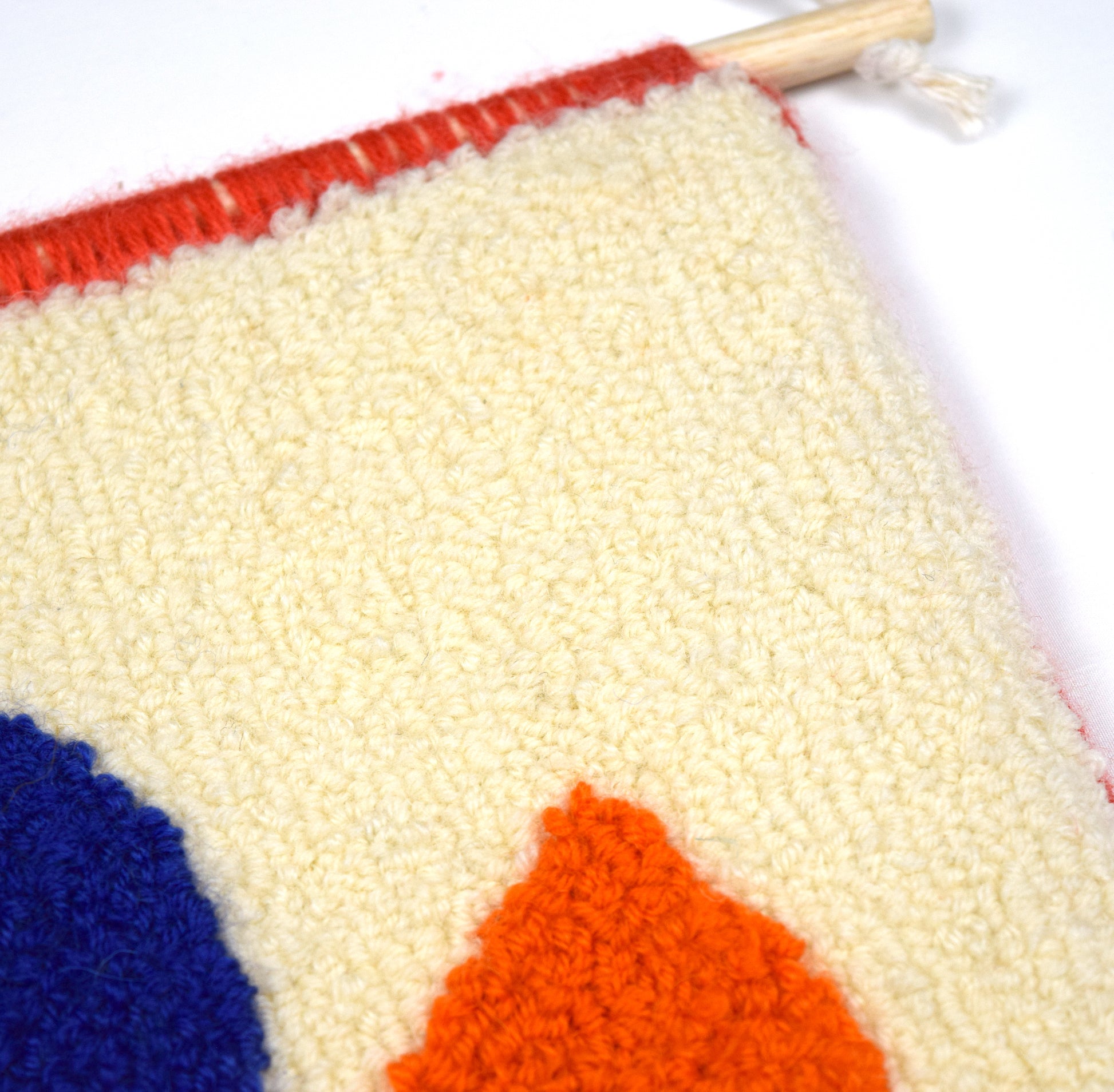 A contemporary hand punched wall hanging, using a simple semi circle with a circle balanced on top of it. Colourful, showcasing the beauty of simplicity, created using Royal Blue, Cream, Coral and Orange British Wool with a hand bound Coral edge close up.