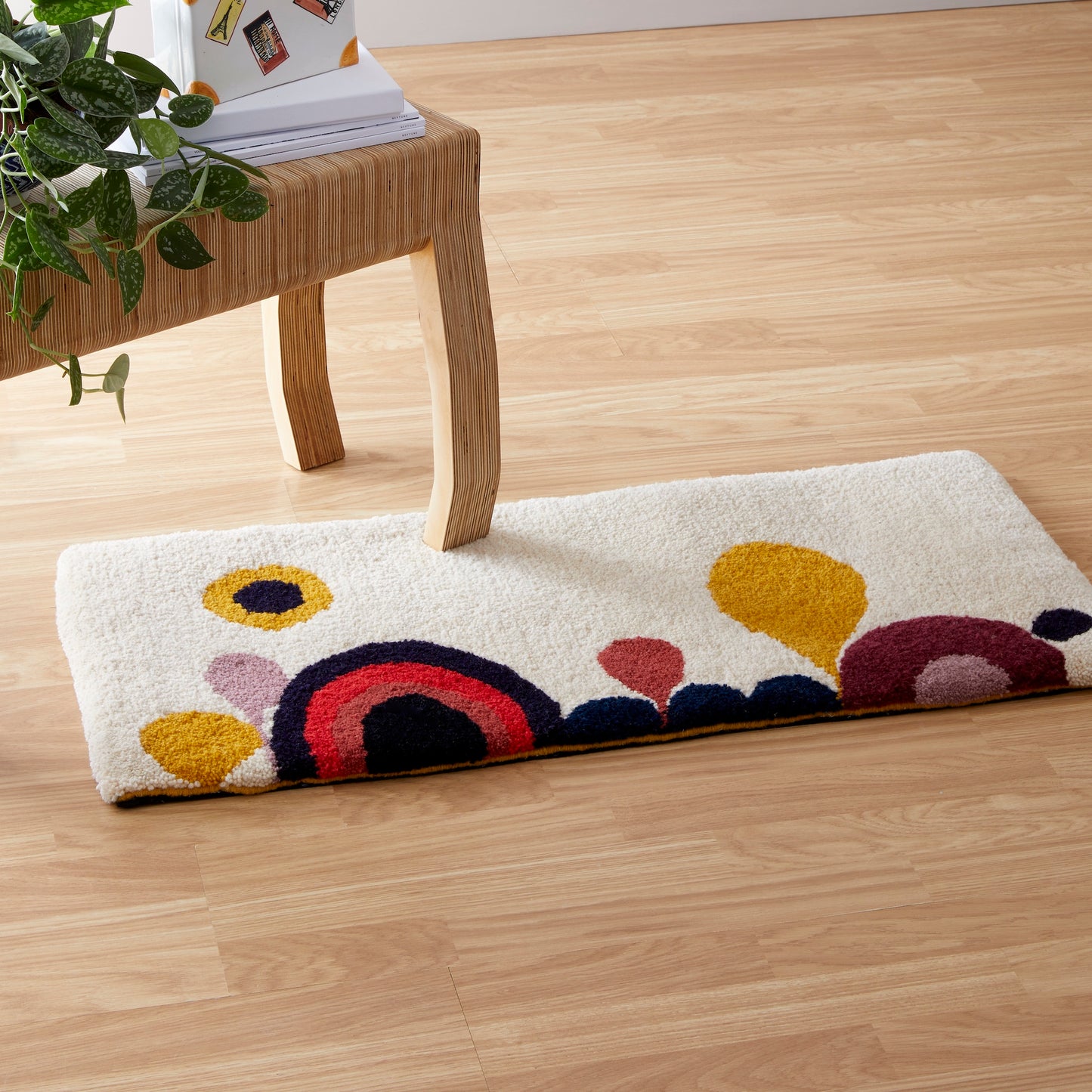 A cartoon-esque Candy Landscape rug runner with rainbows, hills and trees, hand tufted in a mixture of mustard, lilac, cream, red, coral, black, navy and maroon reclaimed yarns. A cut pile finish with hand bound mustard edges.