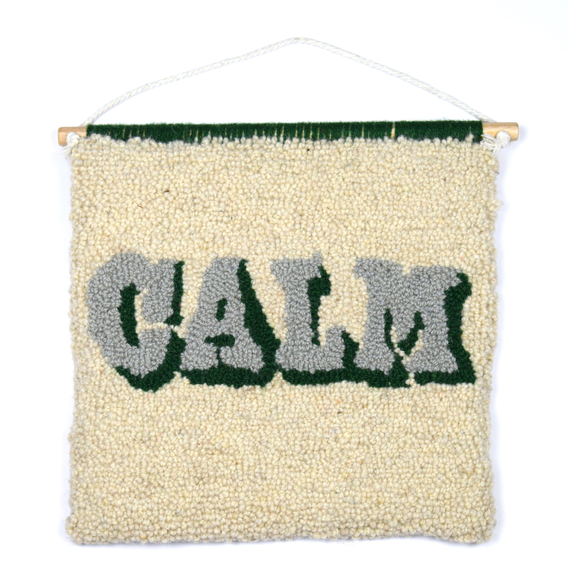 A vintage style typography Wall Hanging with the word CALM soft cream, khaki and green in a loop pile tuft using reclaimed yarn. 