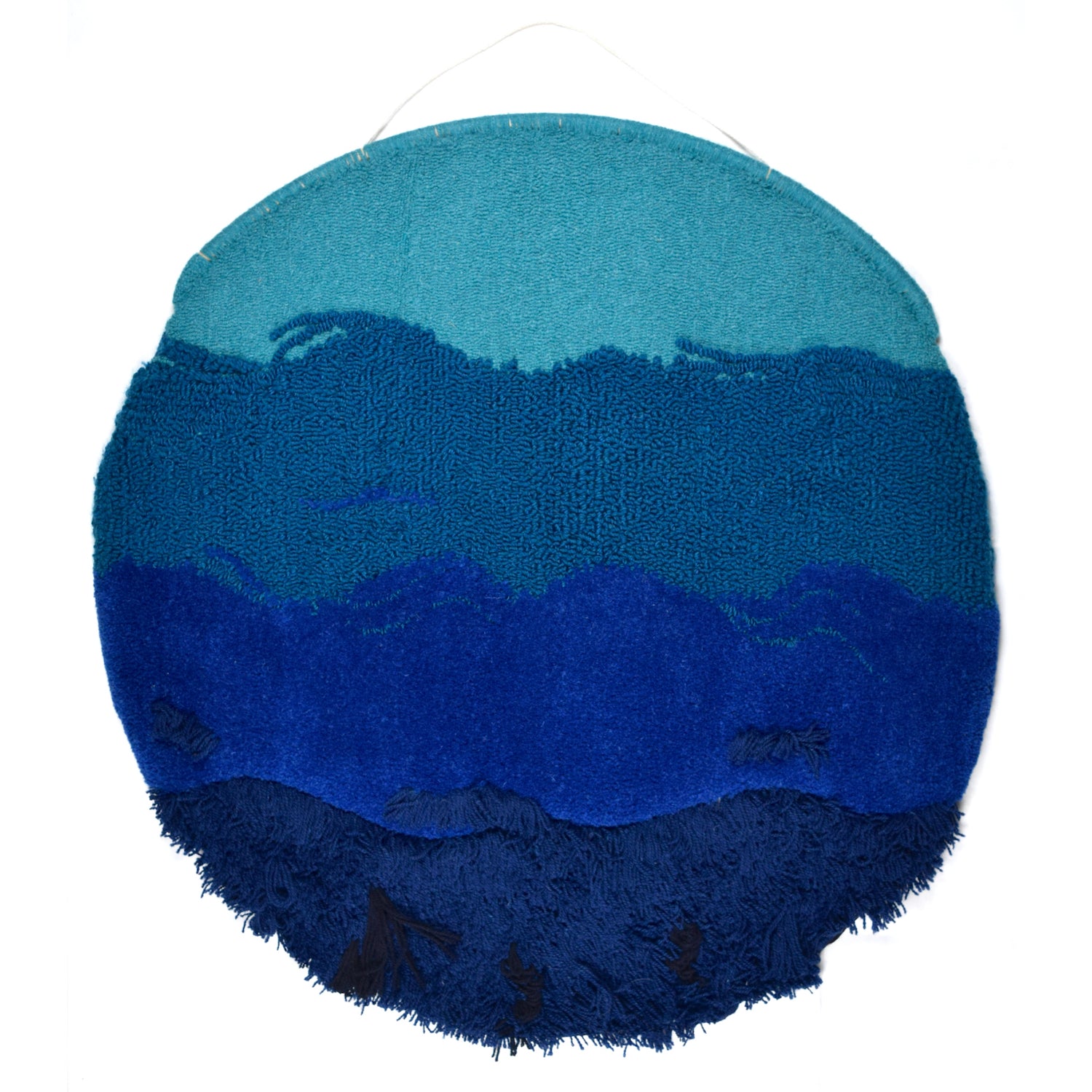 A circular Wall Hanging, ranging from a light turquoise loop pile, blending in to a darker turquoise loop, then royal blue cut pile and navy blue latch hook with additional black finger knitted and crocheted pieces.