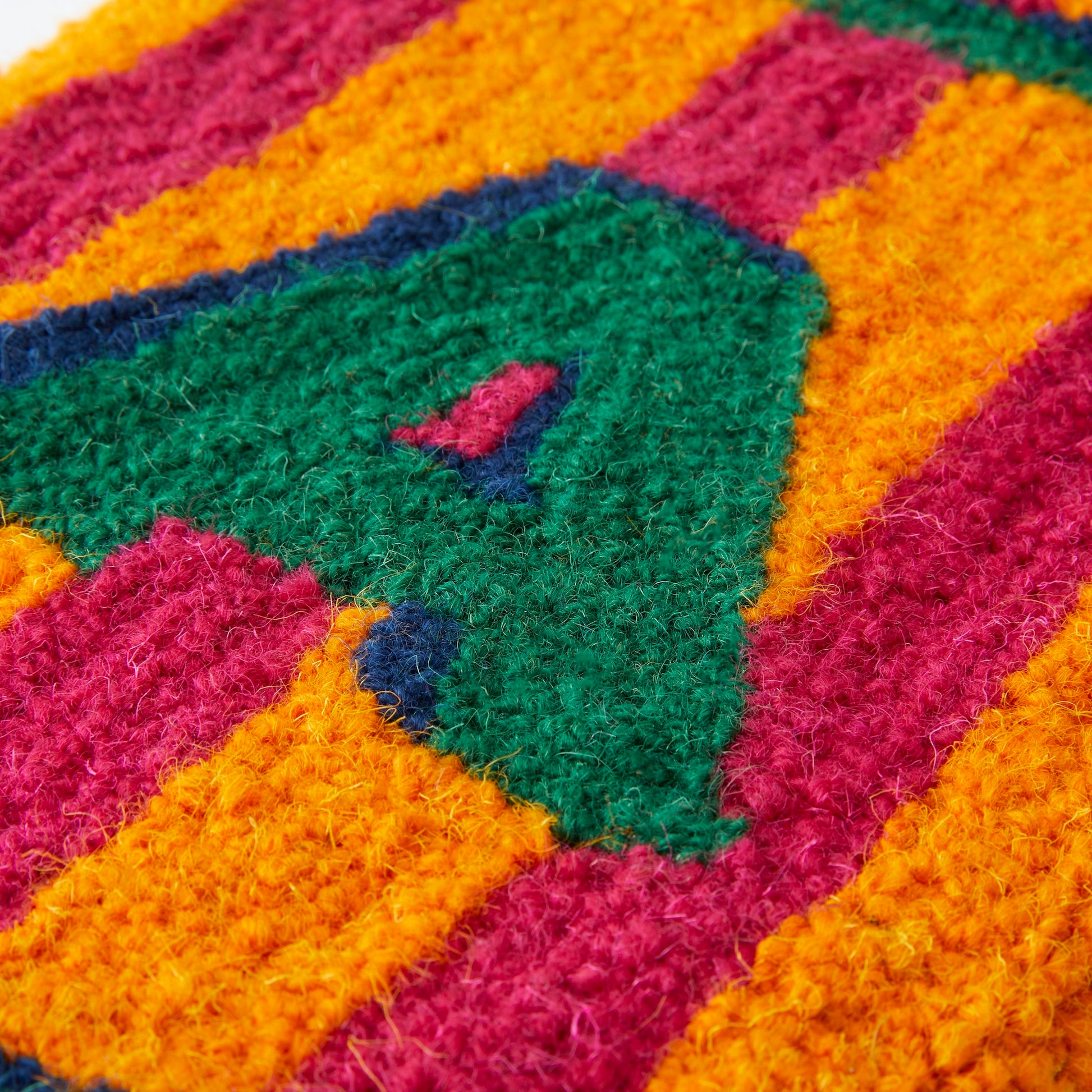 DREAM in a bold shadow text, Green and Navy shadows with a Magenta and Orange striped background in a loop pile using reclaimed yarn close up. 